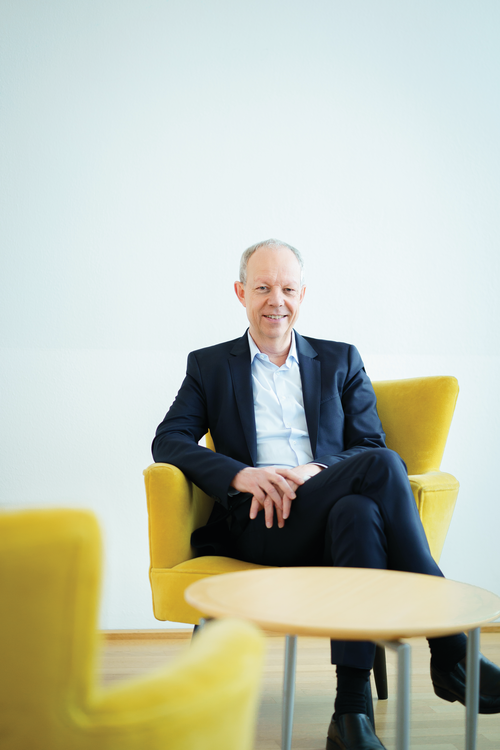 Der ehemalige GLS Bank Vorstandsvorsitzende Thomas Jorberg sitzt auf einem gelben Sessel und lächelt in die Kamera