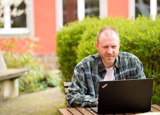 Ein Mitarbeiter sitzt im Innenhof der GLS Bank und schaut in sein Laptop.